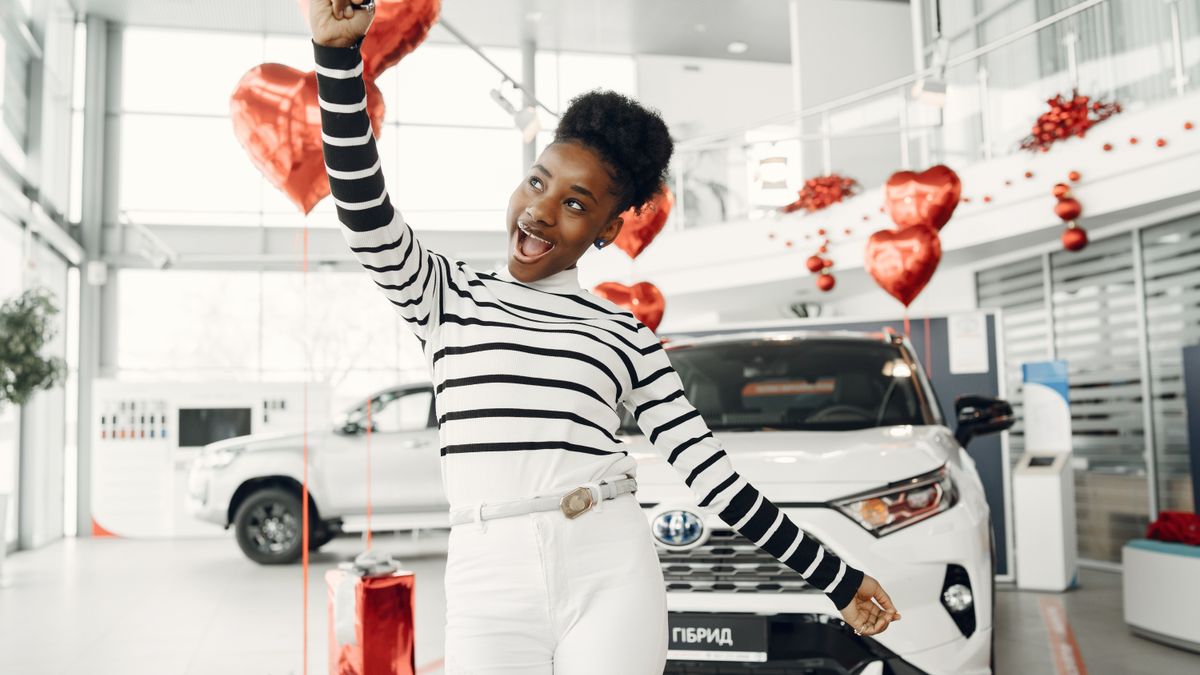 A happy first-time buyer celebrating next to a car in a dealership showroom