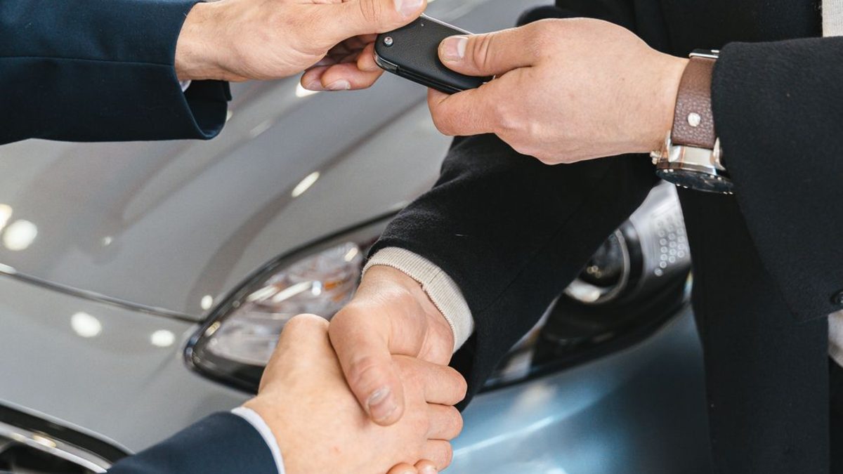 A seller hands over the car keys and shakes hands with the buyer after completing a vehicle sale in New Hampshire
