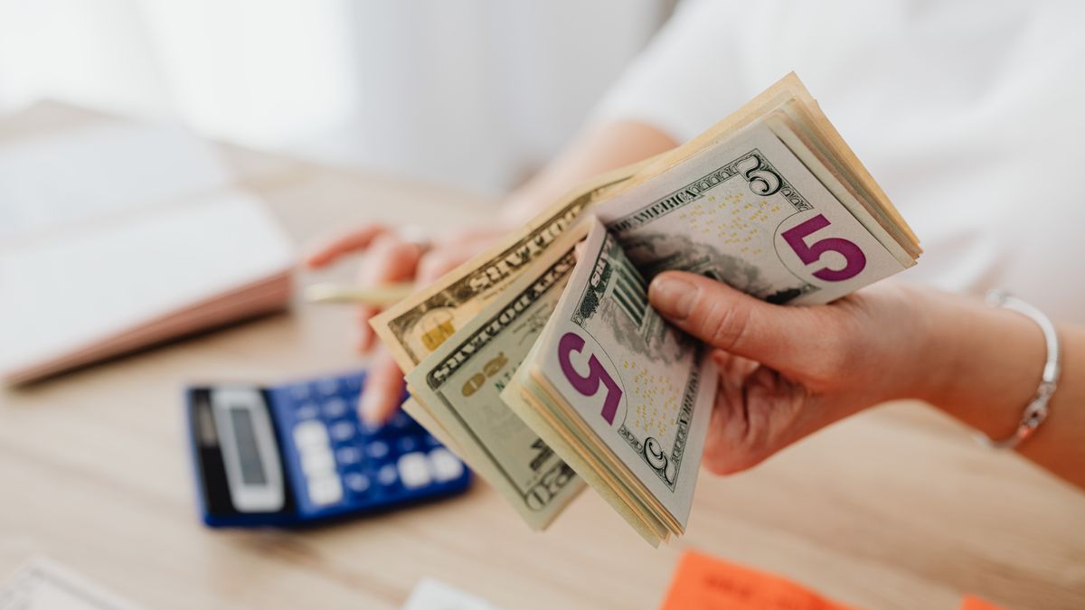 Hands counting US dollar bills next to a calculator — saving a down payment for a used car
