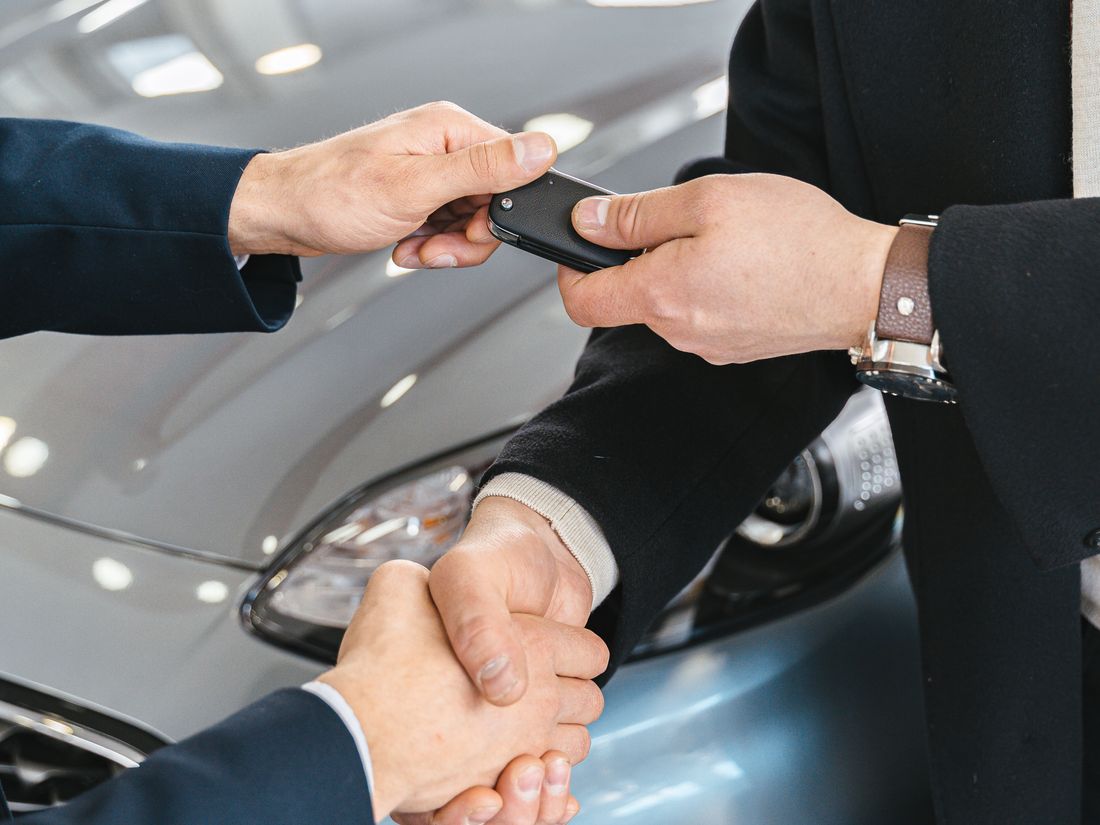 A set of car keys and cash being handed across a desk at a dealership
